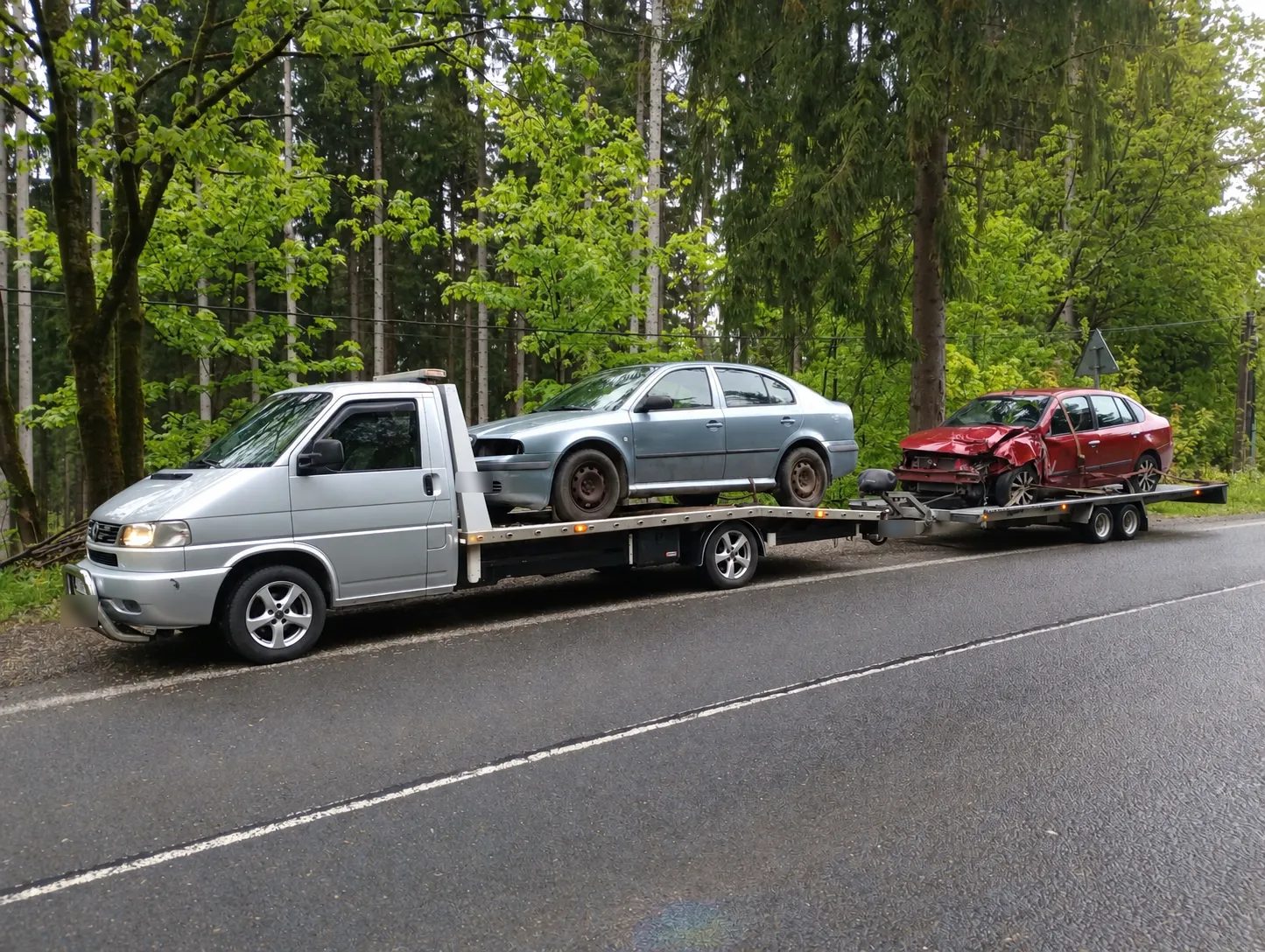 Odťahová VW T4 so Škodou Octavia na plošine a havarovaným červeným autom na prívese v lese