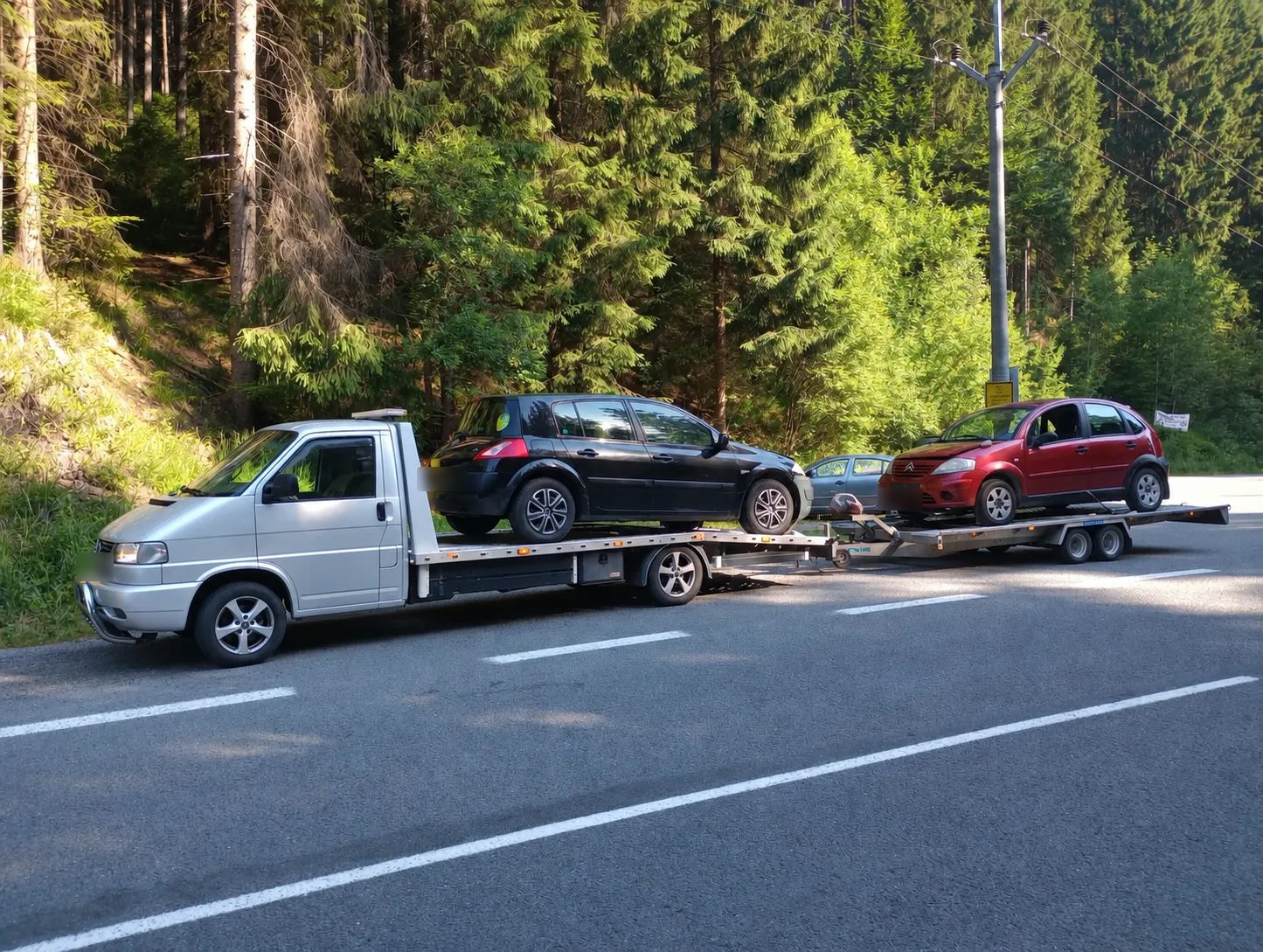 Strieborná odťahová VW T4 s Renaultom Mégane na plošine a Citroënom C3 na prívese pri smrekovom lese