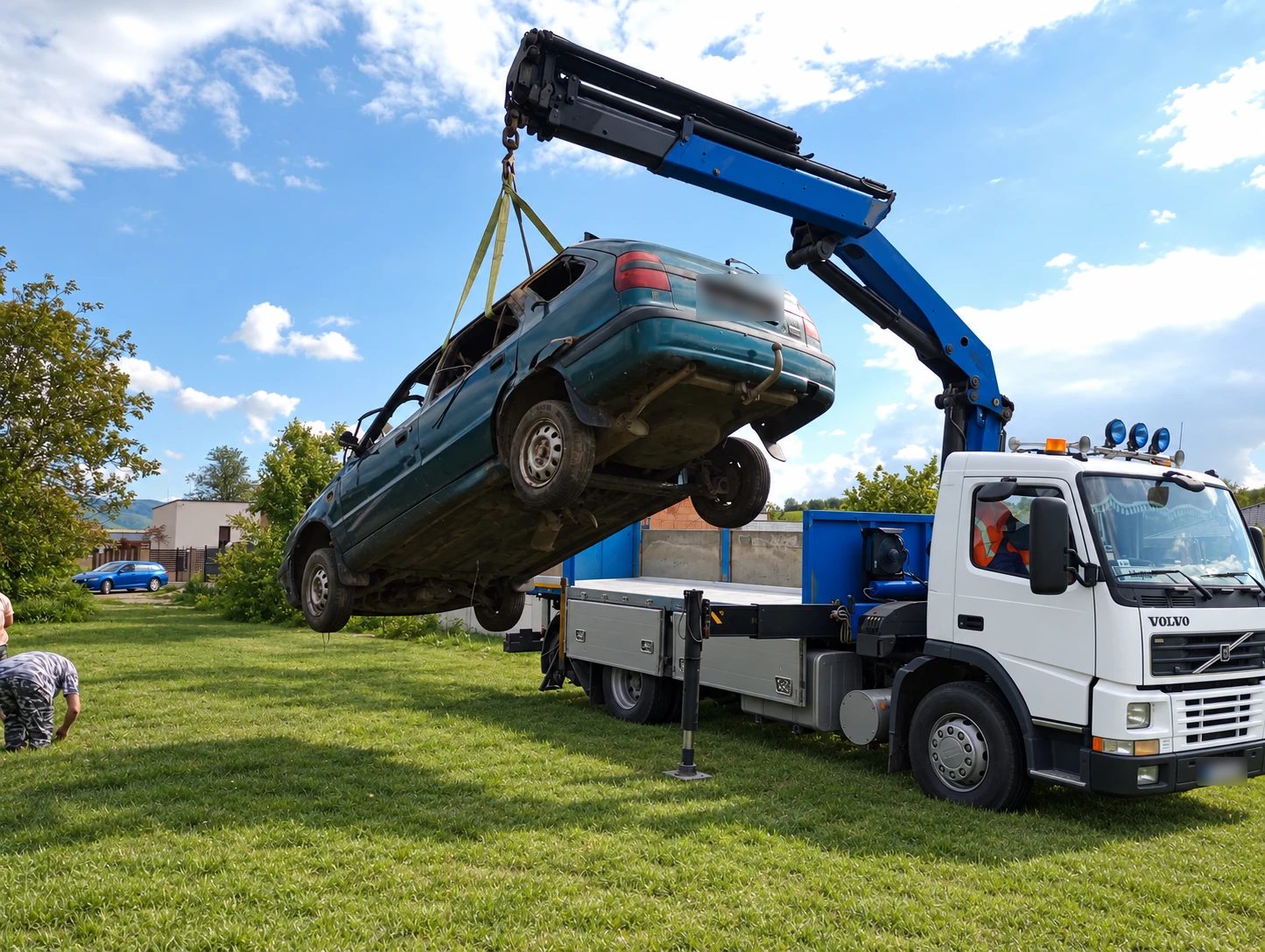 Hydraulická ruka nákladného auta dvíha zelený autovrak z trávnika na korbu